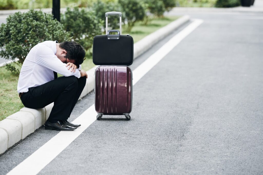 Man sitting beside luggage on a curb after a trip and fall incident on a public sidewalk in California